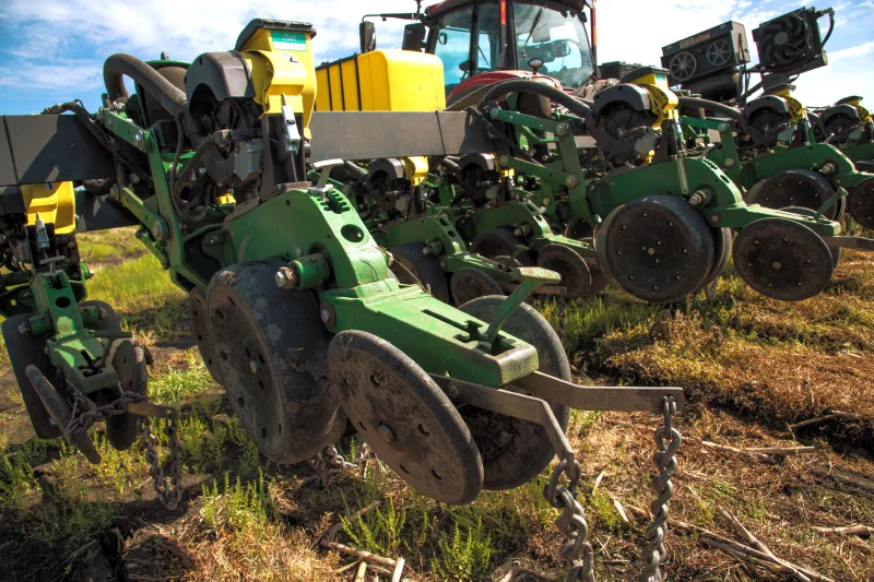 Planter row units in a field, with a red tractor behind, at Frick Farms in northeast Texas.