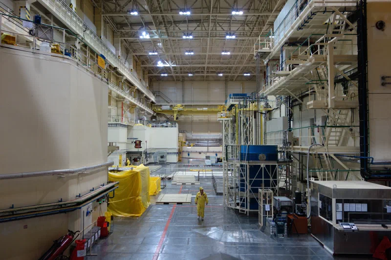 Real photograph inside the reactor hall at the existing Dukovany Nuclear Power Plant in 2012, showing service platforms, an overhead crane, industrial equipment and a worker in yellow clothing.